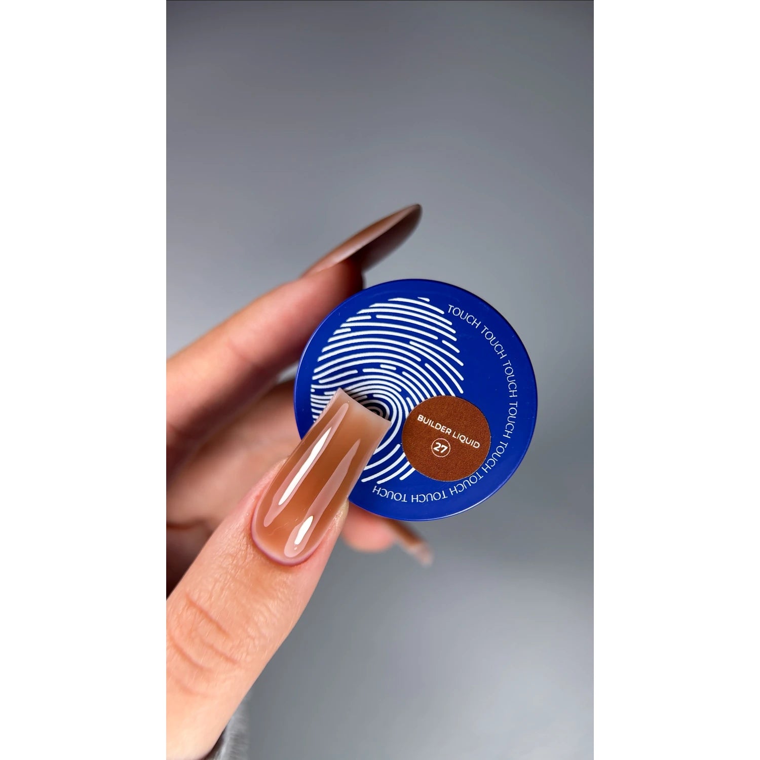 Hand holding a jar of Builder Liquid 27 nail gel, showcasing glossy nude manicure.