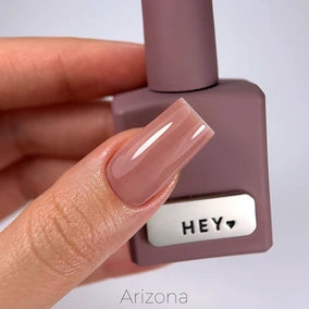 Hand with glossy nude pink gel nail polish holding matching bottle labeled HEY