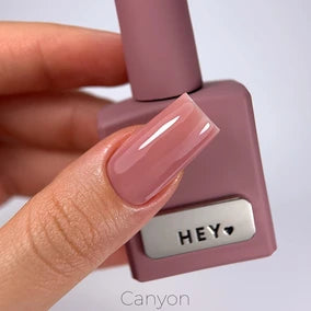 Hand with glossy nude mauve gel nail polish holding matching bottle labeled HEY, ideal for manicure