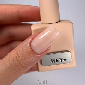 Hand with glossy nude gel manicure holding a bottle of pale pink nail polish