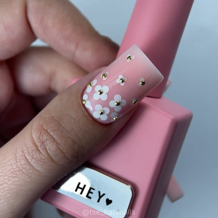 Pink ombre nail with white floral nail art and gold studs, holding pink nail polish bottle