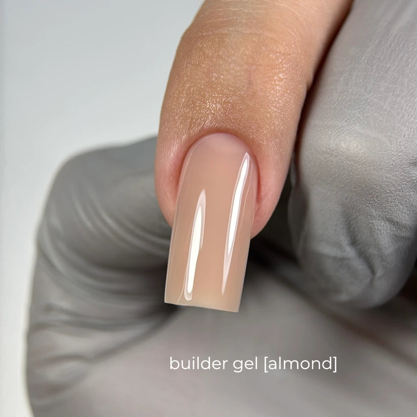 Hand with almond nude builder gel manicure, glossy long square nail, gray glove background