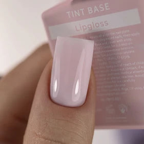 Hand with glossy pale pink UV gel polish manicure, nail polish packaging in background