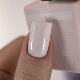 Close-up of a hand with glossy light pink gel nail polish and tint base bottle in background