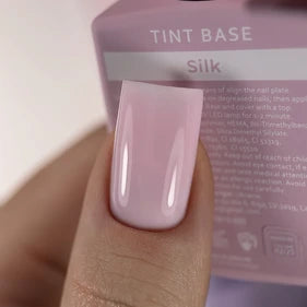 Close-up of a fingernail with glossy light pink gel polish, labeled Tint Base Silk.