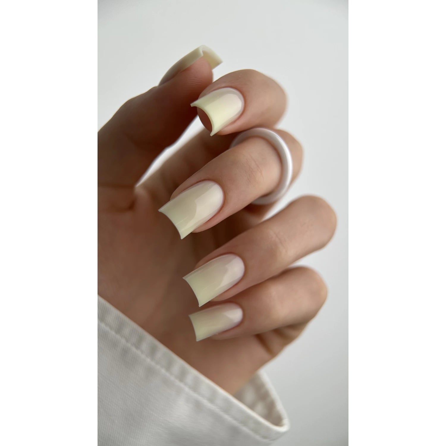 Hand with glossy pale yellow square acrylic nails and white ring, manicure close-up