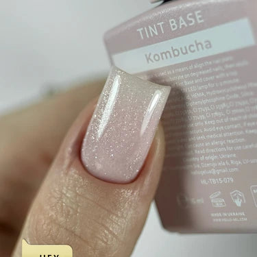 Close-up of a hand with a glossy, light pink glitter gel nail polish labeled Kombucha tint base.