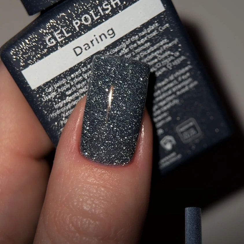 Glittery dark gray gel nail polish on fingernail, labeled Daring, manicure product close-up.