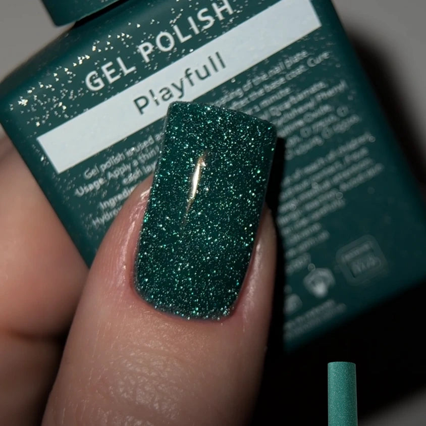 Green glitter gel polish on manicured nail, bottle labeled Playfull in background