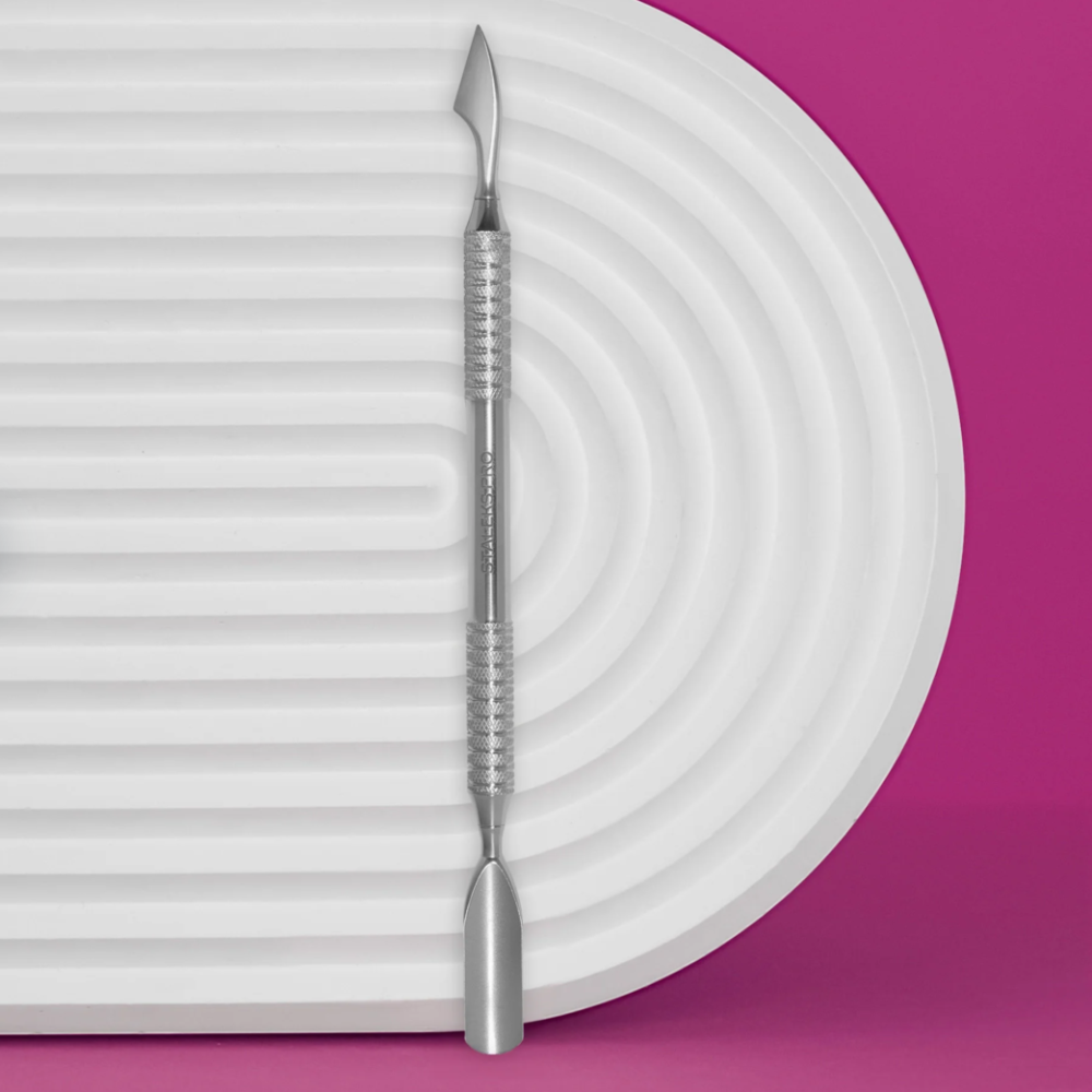 Stainless steel nail cuticle pusher for manicure on white textured tray with pink background