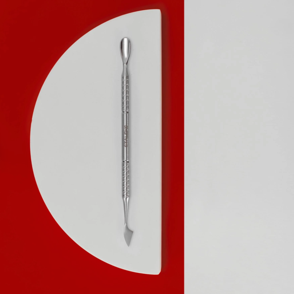 Stainless steel dual-ended cuticle pusher on a modern red and white background, manicure tool