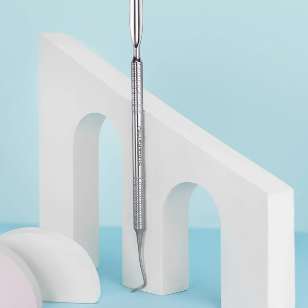 Stainless steel manicure cuticle pusher tool on geometric white and blue background