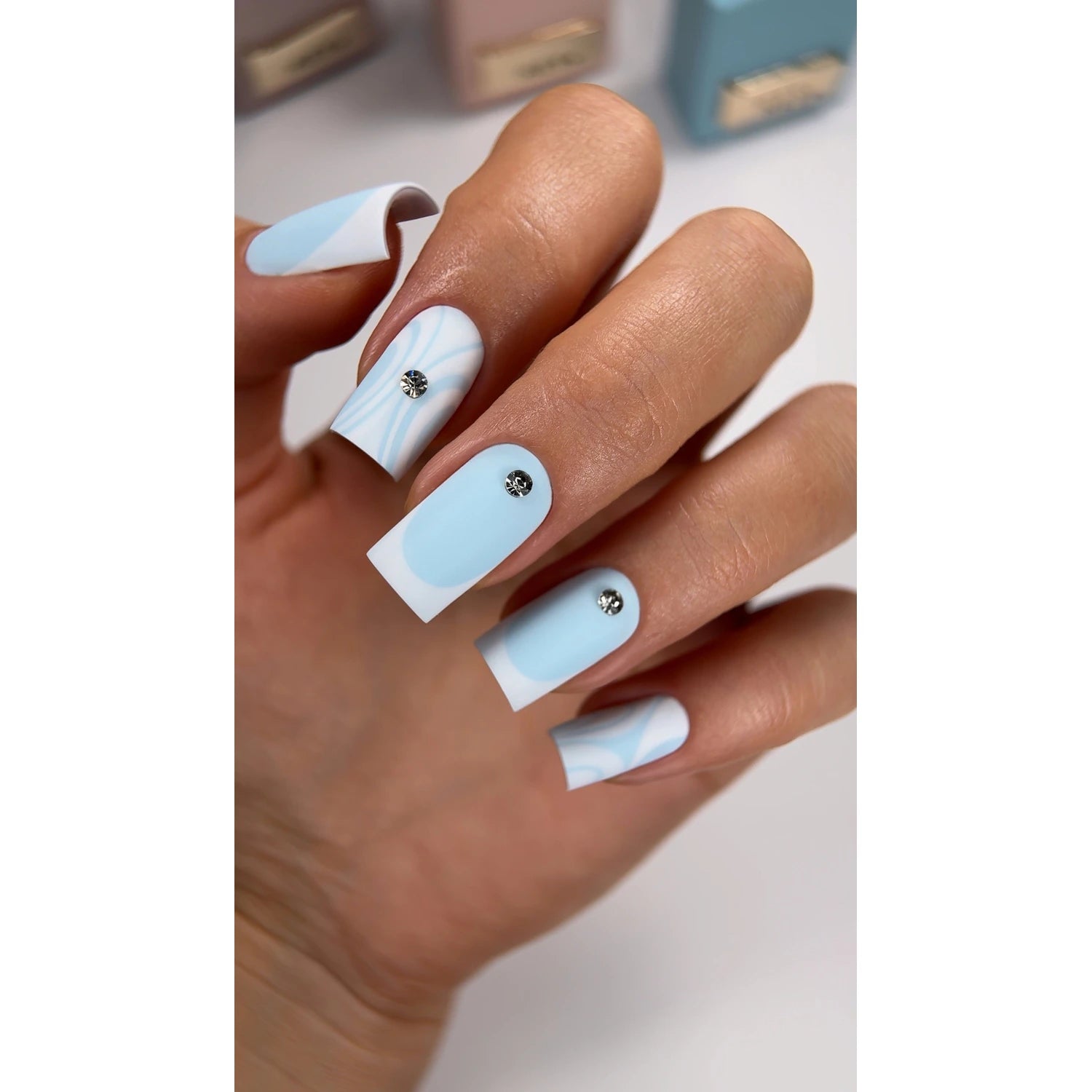 Hand with square blue and white gel nails, rhinestone accents, modern manicure design