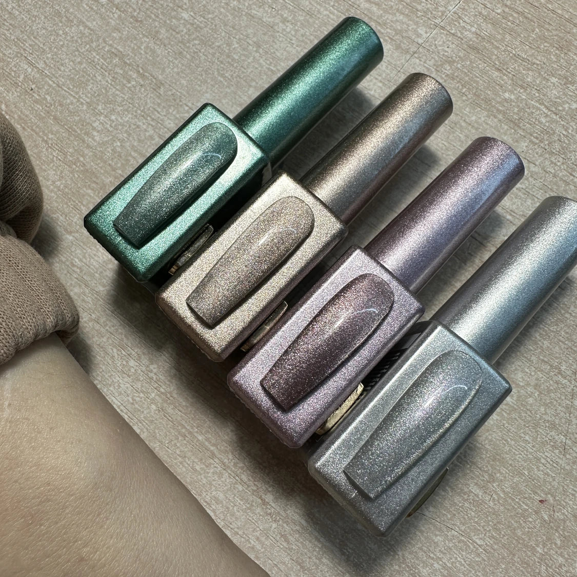 Four metallic shimmer gel nail polish bottles in green, gold, mauve, and silver on a wooden surface