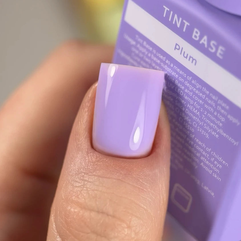 Close-up of a thumb with glossy pastel purple gel nail polish, manicure accessory in background.