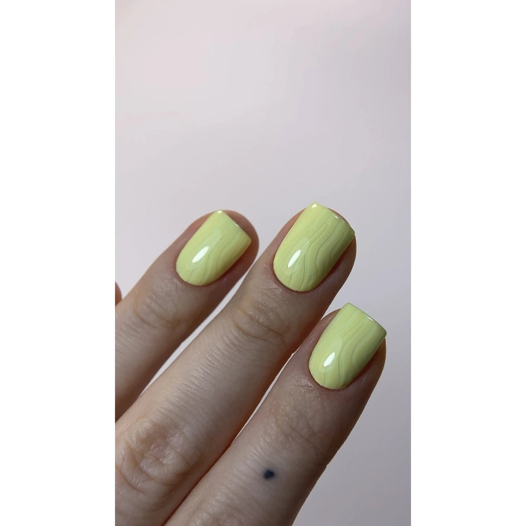 Hand with short square nails in glossy pastel yellow marble nail art design