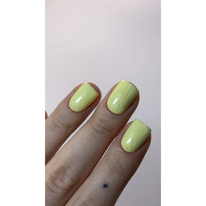 Hand with short square nails in glossy pastel yellow marble nail art design