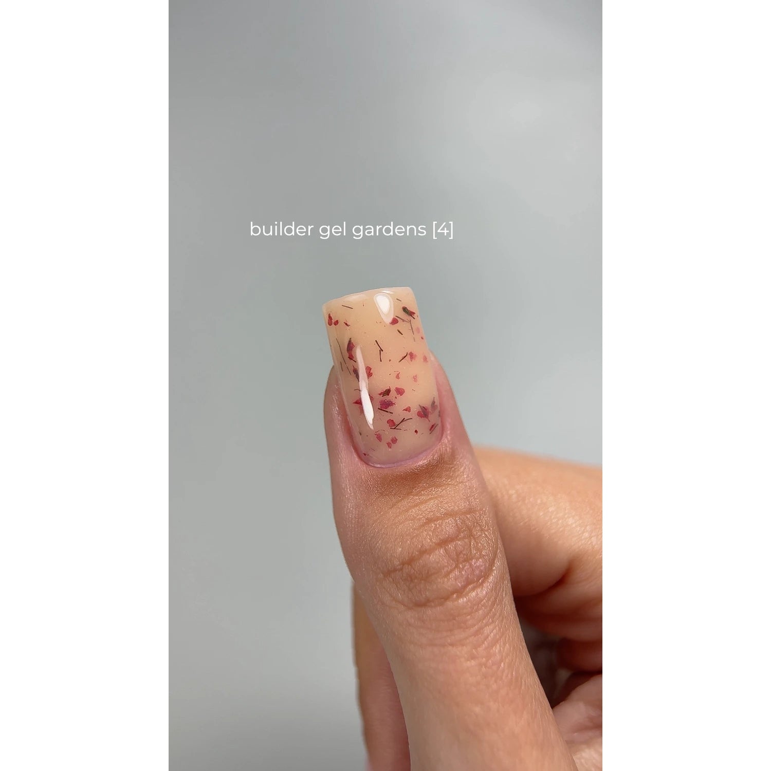 Thumb with nude builder gel manicure featuring red flakes, square nail shape, close-up.