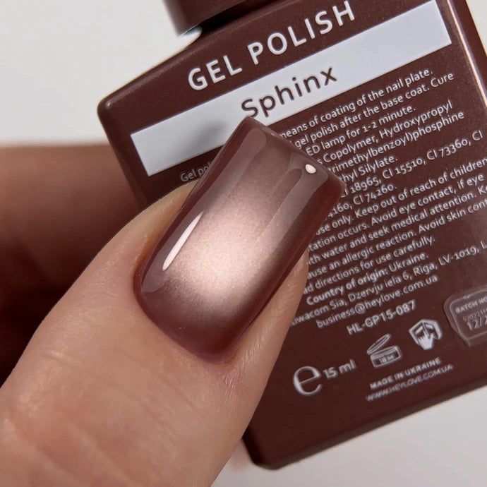 Close-up of a hand showing glossy brown gel nail polish Sphinx with bottle in background