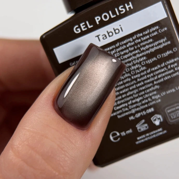 Hand with metallic brown gel polish manicure holding Tabbi gel polish bottle
