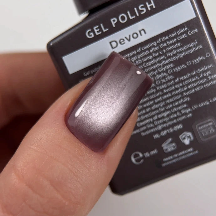 Hand with a shiny mauve gel polish manicure holding a bottle labeled 'Devon' gel nail polish.