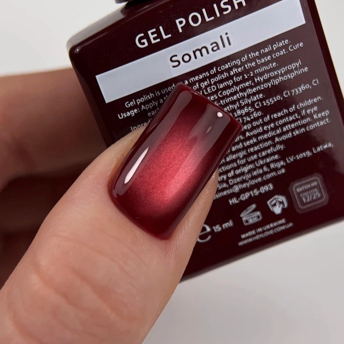 Close-up of a hand with glossy burgundy gel polish manicure, nail polish bottle in background