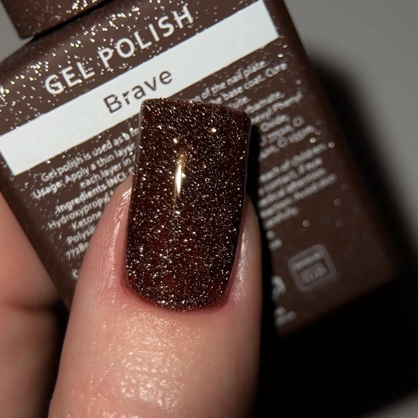 Brown glitter gel polish on fingernail with Brave gel polish bottle in background