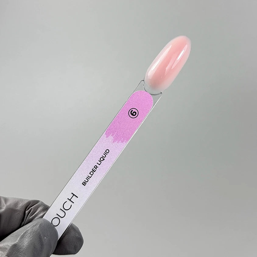 Pink builder gel swatch stick for nails, labeled as builder liquid, held by a gloved hand