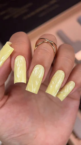 Hand with long square yellow marble nails, gold ring, manicure nail art design