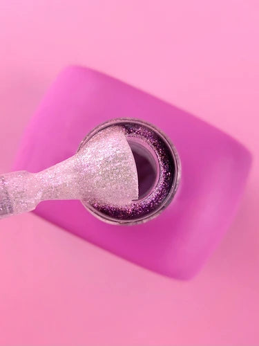 Pink nail polish bottle with silver glitter brush on pink background