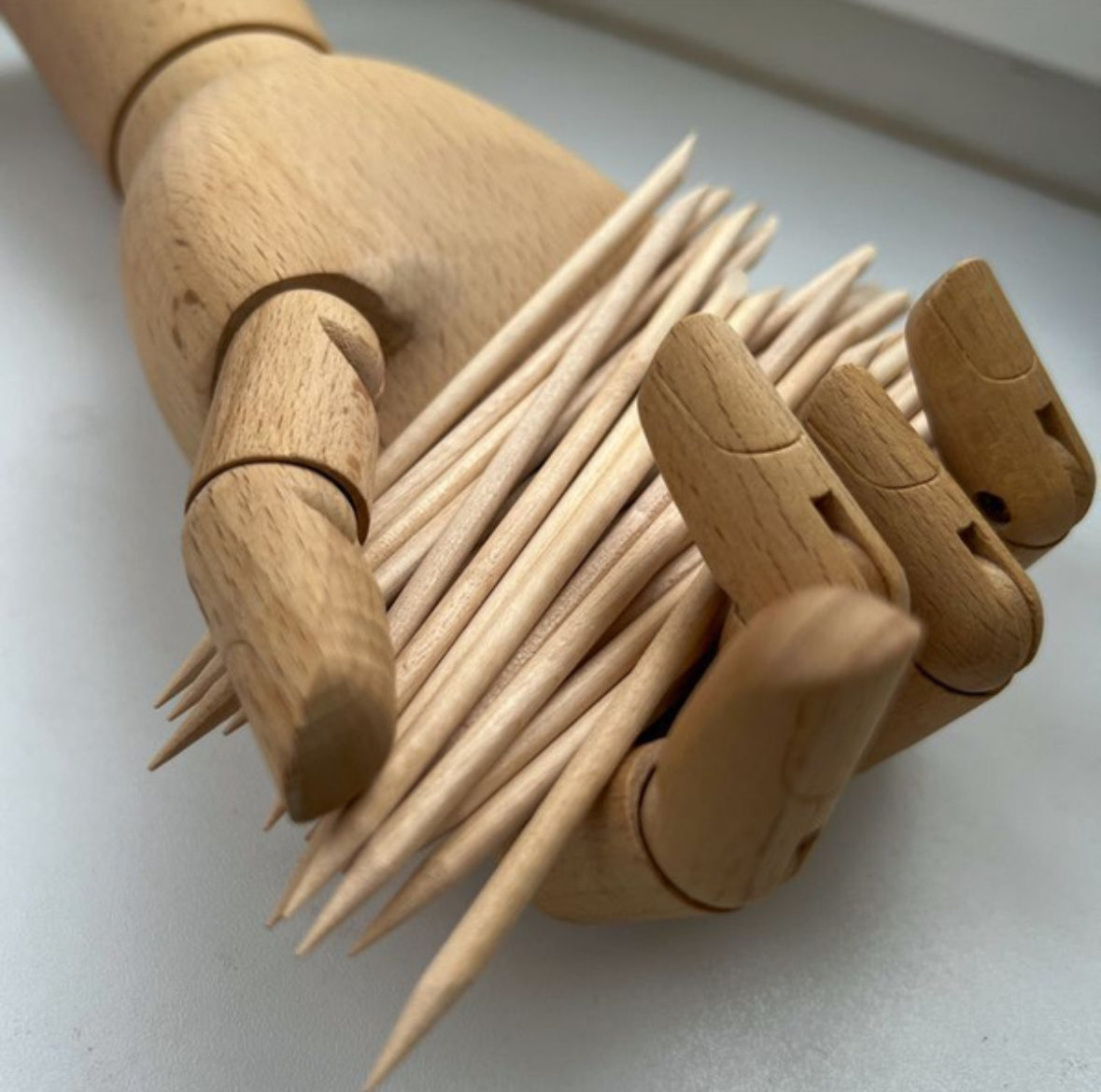 Wooden mannequin hand holding multiple wooden cuticle sticks for manicure