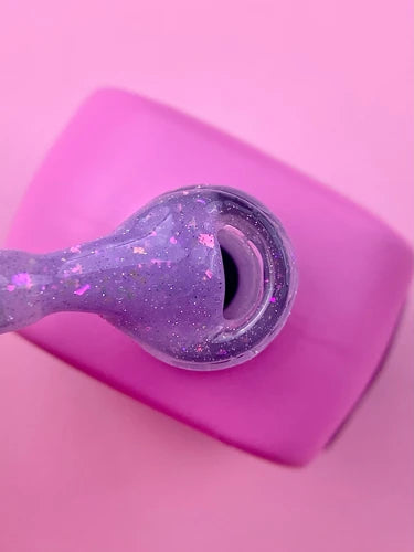 Purple glitter gel nail polish bottle with brush on pink background