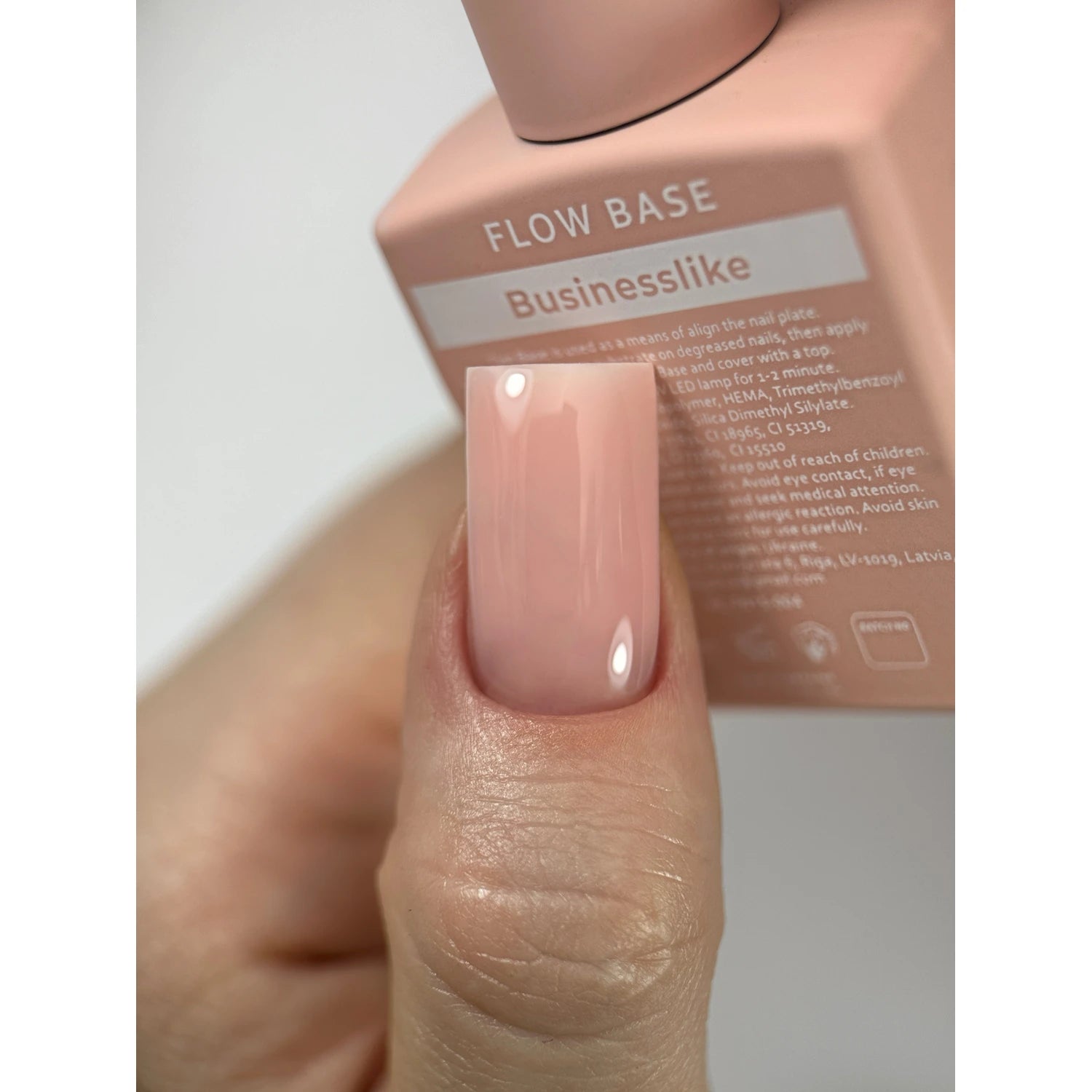 Hand with glossy nude pink gel polish on nail, holding a Businesslike Flow Base bottle