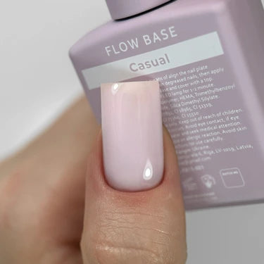 Hand with pastel pink gel nail polish, holding a bottle labeled Flow Base Casual.