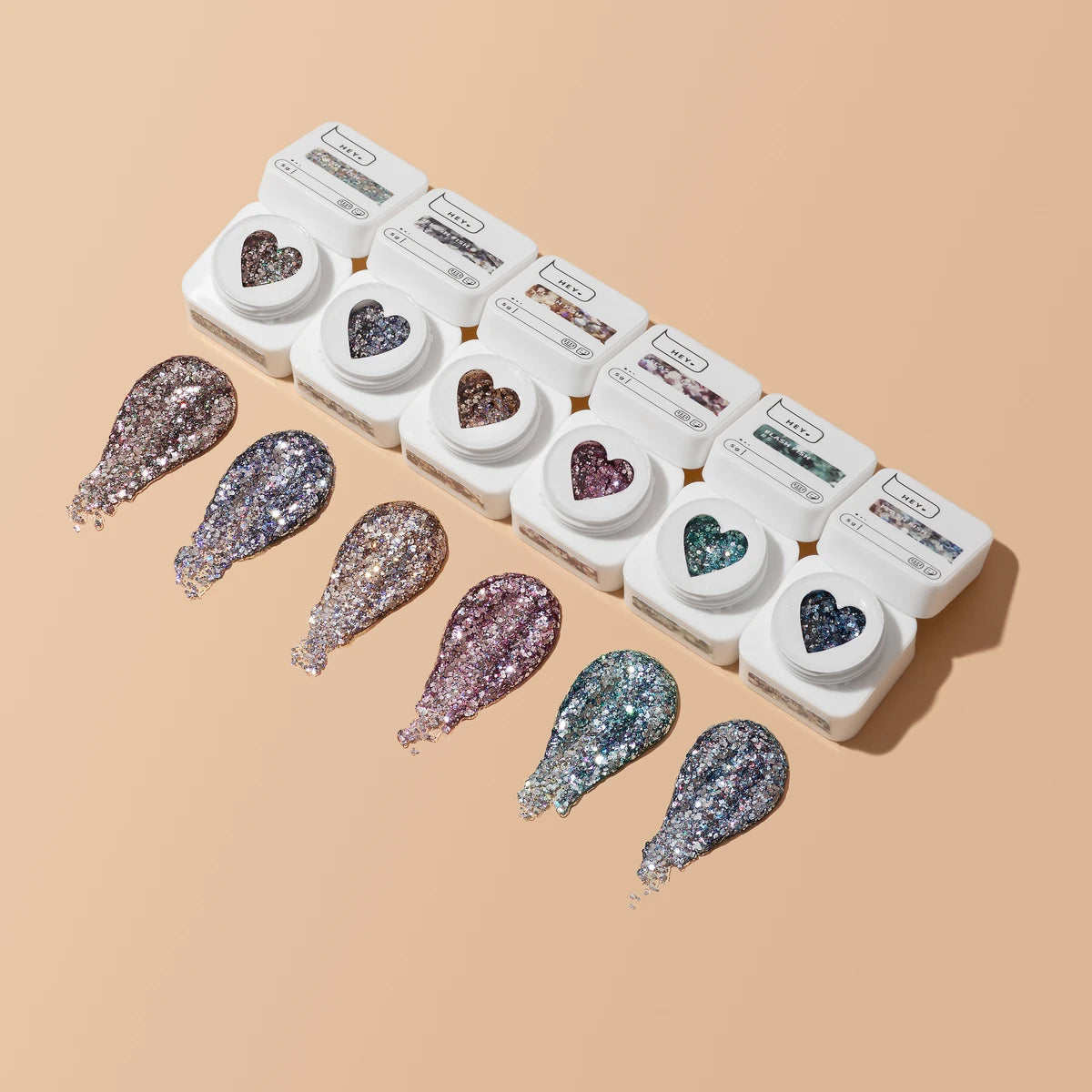 Set of glitter UV gel nail polishes in heart-shaped containers with color samples on beige background