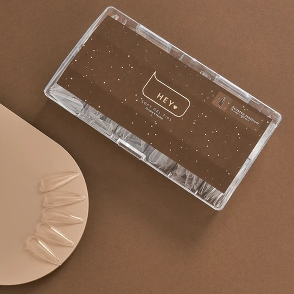 Clear soft gel nail tips in a plastic case on brown background, salon medium style for manicure