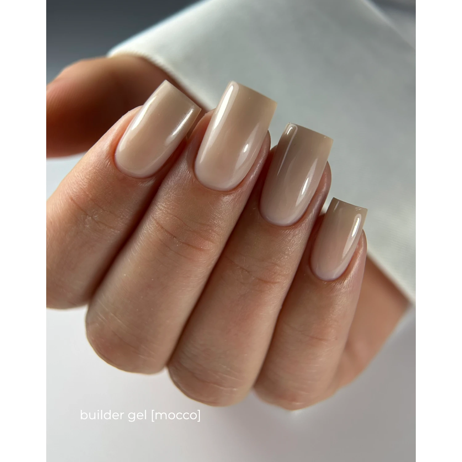 Hand with square nude builder gel nails in mocco shade, professional manicure