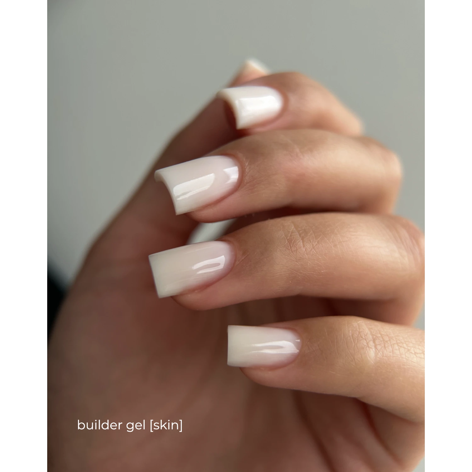 Hand with natural-looking square nude nails, glossy finish, builder gel manicure