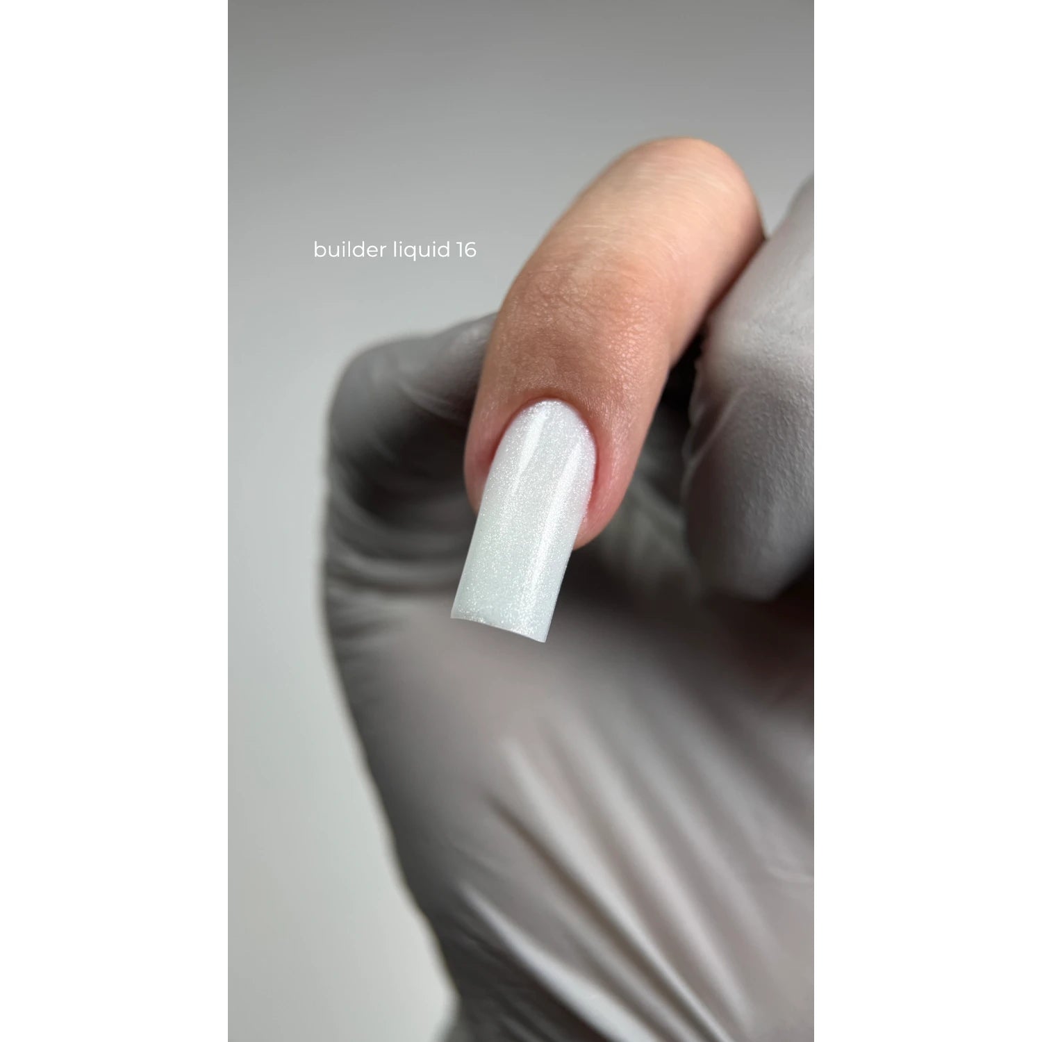 Hand in glove holding a finger with long, shimmery white builder gel acrylic nail