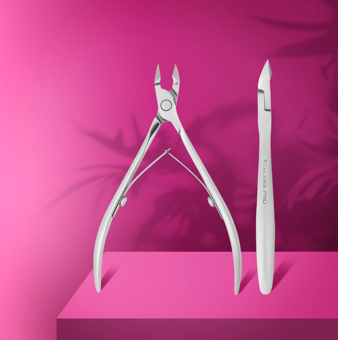 Stainless steel nail cuticle nippers and pusher on pink background for manicure