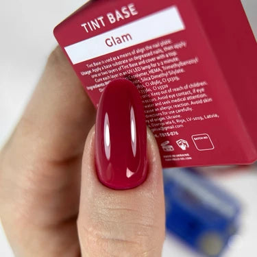 Hand with glossy dark pink gel manicure holding Glam tint base nail polish box