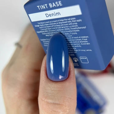 Hand with long nail polished in glossy denim blue tint beside matching nail gel bottle