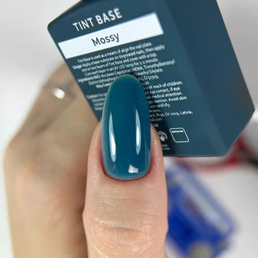 Hand with teal mossy gel nail polish holding tint base bottle, manicure product close-up