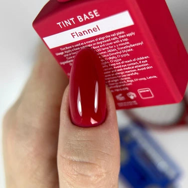 Hand with glossy red gel polish on nail holding Flannel Tint Base bottle for manicure