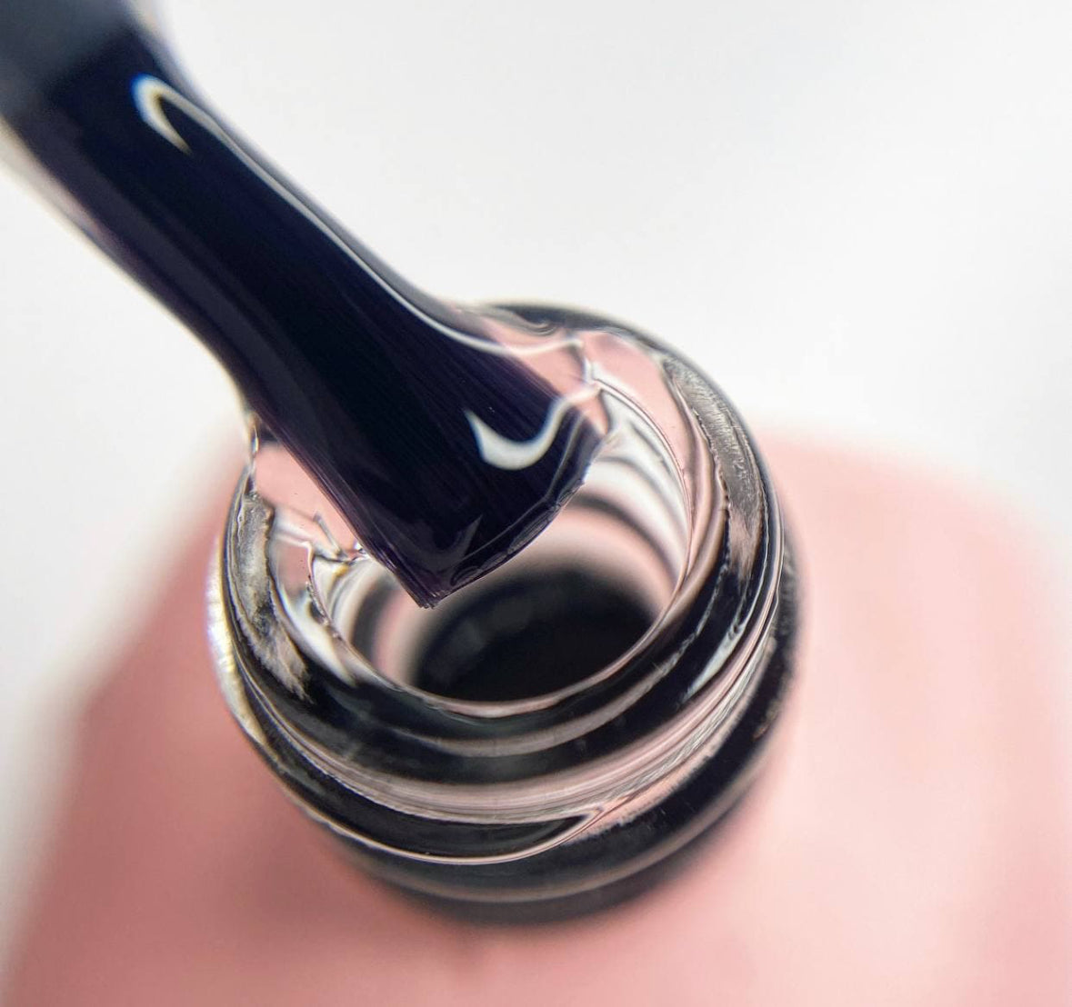 Close-up of a nail polish brush with deep purple gel polish above an open bottle