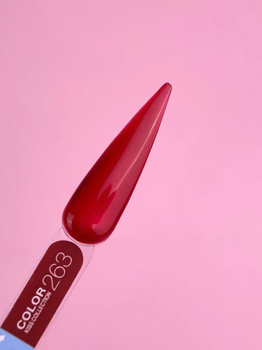 Long almond-shaped nail tip painted glossy deep red, displayed on a pink background
