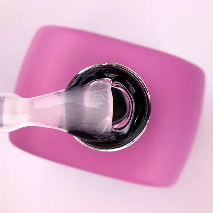 Nail brush dipped in clear UV gel over pink container, manicure product closeup