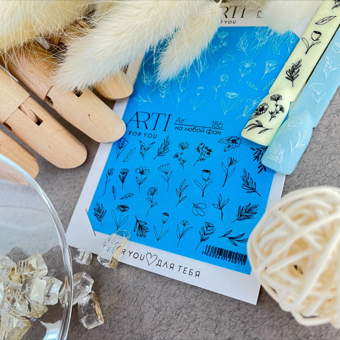 Nail art stickers with black floral designs on a blue sheet, manicure accessories nearby.
