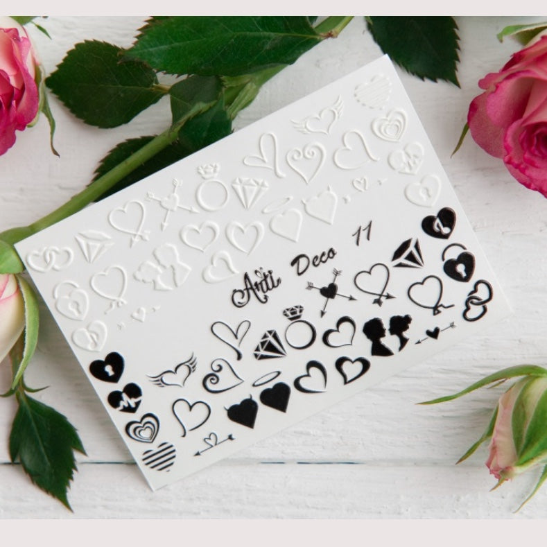 Nail art stickers with heart, diamond ring, and silhouette designs on a white card, roses in background