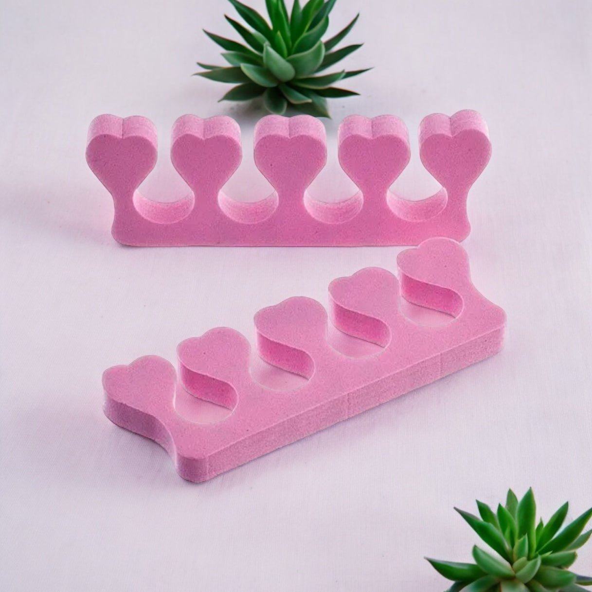 Pink heart-shaped toe separators for pedicure on white background with green succulents